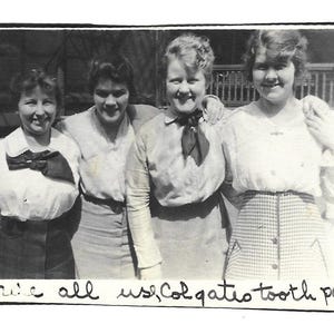 May include: Black and white vintage photograph of four women posing together. They are wearing blouses and skirts. The text at the bottom of the photo reads "we all use Colgate tooth paste."