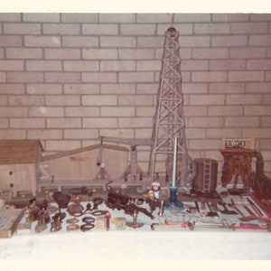 May include: A collection of vintage toy oil derricks and related equipment, including a wooden derrick, a small wooden building, and various metal tools. The word "TOYS" is visible on a small sign.