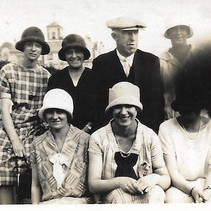 May include: A black and white photo of a group of people wearing hats. The people are standing in front of a building. The people are all smiling.