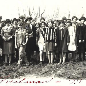 May include: Black and white vintage photograph of a group of people, likely students, standing outdoors. The group is composed of men and women, all dressed in clothing from the early 20th century. The word "Freshman - '27" is written in cursive at the bottom.
