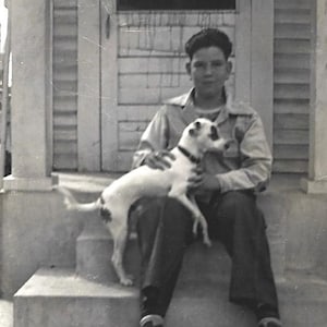 May include: A young person sitting on steps with a white and black dog. The person is wearing a light-colored shirt and dark pants. The dog is sitting on the person's lap.