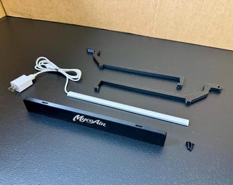May include: A black MycoAir electronic device with a white power cord and plug, accompanied by two black plastic mounting brackets and two small black screws. The device features a rectangular black housing with the white text MycoAir printed on it.