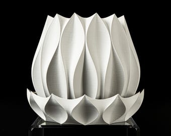 May include: A white, 3D-printed decorative object with a lotus flower design. The object features a series of curved, petal-like shapes that form the main body, and a base with pointed, leaf-like elements. The background is black.