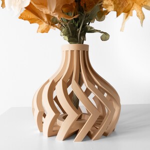 May include: A light brown wooden vase with a unique, open design. The vase has a bulbous shape with vertical, curved slats creating an intricate pattern. The vase holds a bouquet of dried flowers with orange and cream-colored petals.