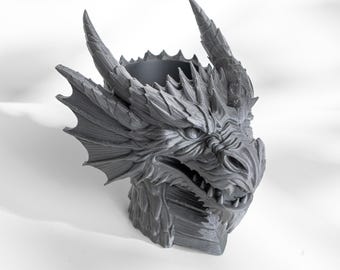 May include: A gray dragon head planter with detailed scales, horns, and a textured surface. The planter has a wide opening for plants and is designed to resemble a fierce dragon. The dragon head is a decorative item.