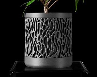 May include: A modern, cylindrical planter with a dark gray, organic pattern. The planter holds a small green plant with multiple branches and leaves. The planter sits on a clear, reflective surface against a black background.