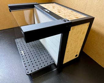 May include: A black rectangular enclosure featuring a perforated base plate and a clear front panel. The top and side panels are decorated with a light-colored pattern of scientific icons, including beakers, atoms, and microscopes, with the text 'Riser' visible.