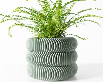 May include: A green, stacked planter with a ribbed design, holding a vibrant green plant. The planter has a unique, modern aesthetic, perfect for indoor or outdoor use. The plant's delicate leaves contrast with the planter's structured form.