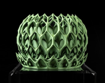 May include: A light green, spherical decorative object with a honeycomb-like pattern. The object has a series of interconnected, geometric shapes, creating an open, lattice-like structure. The object is displayed on a clear, reflective surface against a black background.
