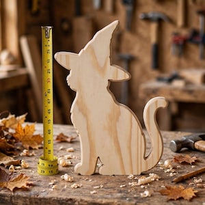 Peut inclure: Une découpe en bois clair représentant un chat portant un chapeau de sorcière, placée à côté d'un mètre ruban jaune indiquant une hauteur d'environ 30 cm. La figurine de chat en bois présente une surface lisse avec des veines de bois visibles.