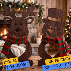 May include: Two dark brown wooden cutouts, one shaped like a reindeer and one like a snowman, both wearing red and green striped scarves. Each figure features a heart-shaped cutout in the center. Text reads: DIGITAL DOWNLOAD! 18IN PATTERN PDF SVG DXF.