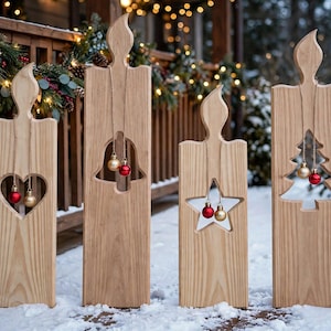 May include: Four light-colored wooden candle-shaped decorations with flame-shaped tops. Each features a cutout shape: a heart, a bell, a star, and a Christmas tree. Small red and gold spherical ornaments hang from twine inside each cutout.