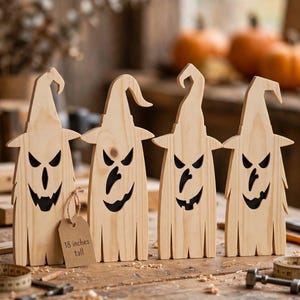 May include: Four light-colored wooden ghost figures wearing pointed hats with cut-out facial features. Each figure has a jagged bottom edge and a brown paper tag attached to the first ghost that reads 18 inches tall. The figures stand upright.