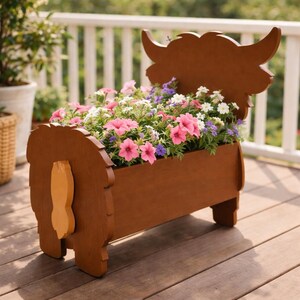 Op de afbeelding: Een bruine houten bloempot in de vorm van een Schotse Hooglander, gevuld met roze, paarse en witte bloemen. De bloempot heeft hoorns en een staart, ideaal voor buitendecoratie.