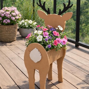 May include: A decorative deer-shaped planter made of light brown wood, filled with colorful flowers. The planter has black antlers and a white tail detail. The flowers include pink, purple, and white blooms, creating a vibrant display.