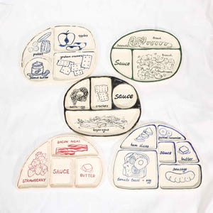 Pode incluir: Um conjunto de cinco pratos de cerâmica esbranquiçada, cada um com vários compartimentos e ilustrações desenhadas à mão de vários alimentos. Os pratos apresentam imagens de maçãs, picles, manteiga de amendoim, bacon e muito mais. A palavra "molho" está escrita em vários pratos.