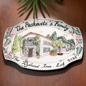 Puede incluir: Una fuente de cerámica blanca con una ilustración pintada a mano de una casa, árboles y montañas. La fuente está decorada con detalles florales verdes y rojos e incluye el texto "The Paskewitz's Family" y "The Ryland Inn, Est 2026".