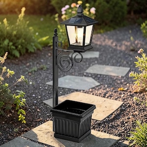 Könnte beinhalten: Schwarze Solar-Außenlaterne mit dekorativem geschwungenem Arm und quadratischer Pflanzgefäßbasis. Die Lampe hat einen schwarzen Rahmen mit klaren Glasscheiben und ein Solarpanel oben. Der Pflanzkübel hat eine quadratische Form mit vertikalen Linien.