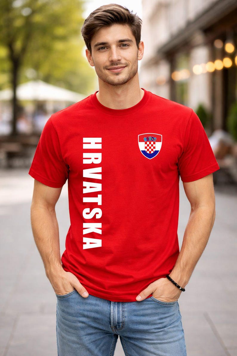 May include: Red t-shirt with the word "HRVATSKA" in white vertical text on the left side. A Croatian coat of arms is on the right chest. The shirt is worn with blue jeans.