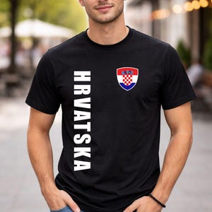 May include: Black t-shirt with the word "HRVATSKA" in white vertical text on the left side. A Croatian coat of arms is on the right chest. The shirt is short-sleeved.
