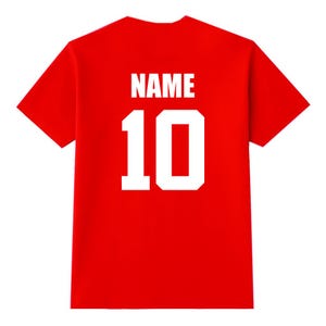 May include: A red t-shirt with the word "NAME" and the number "10" printed in white block letters on the back. The shirt is a solid red color and has short sleeves.