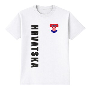 May include: White t-shirt with the word "HRVATSKA" printed vertically in black on the left side. A Croatian coat of arms is on the right chest. The coat of arms is red, white, and blue.