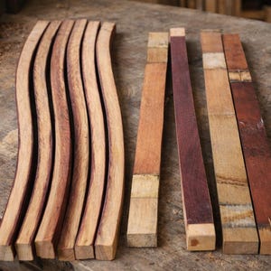 May include: A collection of wooden barrel staves and planks in various shades of brown and red. The curved staves are arranged in a row, while the planks are straight and rectangular. The wood appears to be freshly cut and ready for use.
