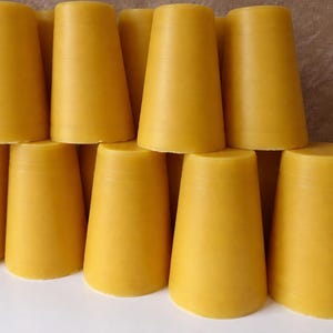 May include: A collection of yellow, cone-shaped blocks, possibly wax or a similar material, are stacked together. The objects have a smooth surface and a slightly tapered design. The color is a warm, golden yellow.
