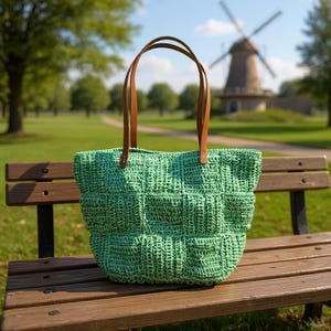 Bolsa de ombro artesanal em fio de papel com motivo verde e alça de couro estruturada.