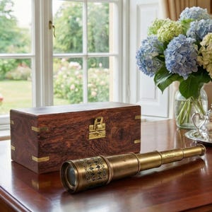 Peut inclure: Un télescope en laiton avec des détails complexes est posé sur une table en bois poli. Une boîte en bois avec des accents en laiton est derrière le télescope. Un vase d'hortensias bleus et verts est en arrière-plan.