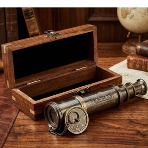 Peut inclure: Un télescope en laiton vintage avec une boussole, posé sur une surface en bois à côté d'une boîte en bois ouverte. Le télescope porte l'inscription "DOLLOND LONDON". La boîte est doublée de tissu noir.