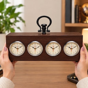 May include: A rectangular dark brown wooden desk clock featuring four circular clock faces with silver bezels. Each face displays a different city name: New York, London, Paris, and Singapore. A black metal handle is attached to the top center.