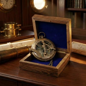 Pode incluir: Uma bússola de latão vintage com um relógio de sol, apresentada em uma caixa de madeira aberta forrada com veludo azul. A bússola é detalhada com marcações intrincadas e uma corrente. Um telescópio e pergaminho enrolado também são visíveis.