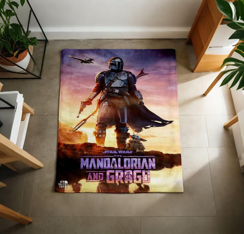 Pode incluir: Uma manta retangular com tema Star Wars com The Mandalorian e Grogu. A manta exibe uma cena com o Mandaloriano segurando um blaster, Grogu e uma nave espacial contra um fundo de p&ocirc;r do sol. As palavras "The Mandalorian and Grogu" s&atilde;o impressas.