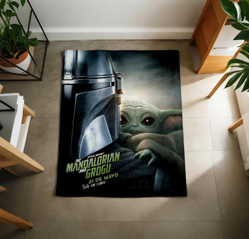 Pode incluir: Um cobertor retangular com tema Star Wars com o capacete do Mandaloriano e Grogu. O cobertor tem o texto "THE MANDALORIAN AND GROGU" em verde e branco, com texto adicional em espanhol. O cobertor est&aacute; em um ch&atilde;o de ladrilhos.