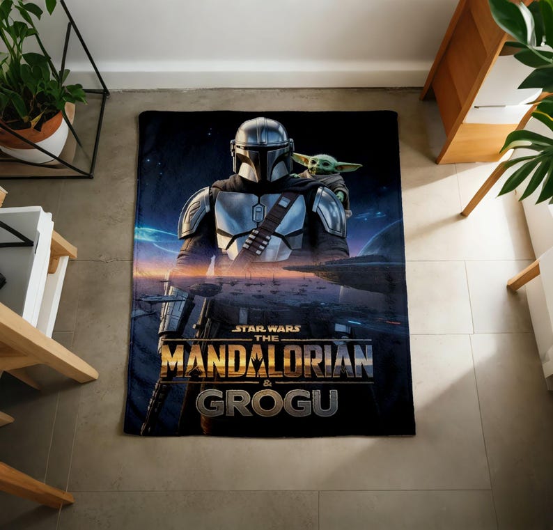 Pode incluir: Um cobertor preto com o Mandaloriano e Grogu de Star Wars. O Mandaloriano est&aacute; em armadura prateada, e Grogu est&aacute; em seu ombro. O cobertor tem as palavras "STAR WARS THE MANDALORIAN & GROGU" em letras douradas.