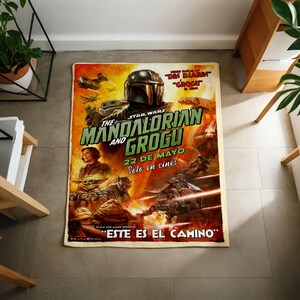 Pode incluir: Um tapete retangular com o cartaz do filme "The Mandalorian and Grogu" de Star Wars. O tapete apresenta um design vibrante com personagens e texto em ingl&ecirc;s e espanhol. O tapete &eacute; retangular e parece ser feito de um material macio.