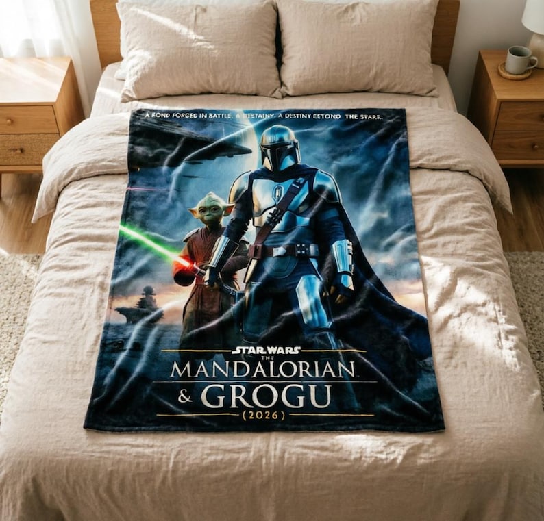 Pode incluir: Um cobertor macio com The Mandalorian e Grogu de Star Wars. O cobertor tem um fundo azul e preto com o texto "STAR WARS THE MANDALORIAN & GROGU (2026)". O cobertor est&aacute; em uma cama.
