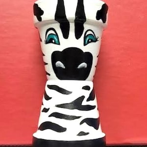 以下が含まれることがあります： 手描きのゼブラ柄のセラミック植木鉢。 植木鉢は白地に黒い縞模様で、ゼブラの顔（青い目と黒い鼻を含む）が描かれています。 ベースは黒です。