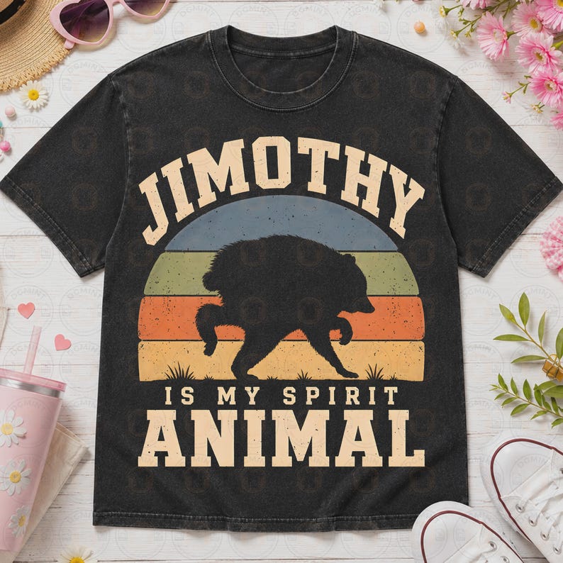 May include: A black short-sleeve t-shirt featuring a graphic of a black bear silhouette centered within a vintage-style sunset of blue, green, orange, and yellow stripes. The text reads JIMOTHY IS MY SPIRIT ANIMAL in a bold, light-colored font.
