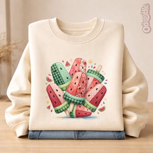 Puede incluir: Sudadera de color crema con un gráfico colorido de paletas de sandía. Las paletas presentan patrones rojos y verdes, incluyendo lunares, cuadros y diseños florales. El diseño incluye rodajas de sandía y pequeños soles.