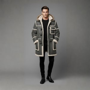 May include: A grey shearling coat with a fur-lined hood and white trim. The coat has toggle closures and multiple pockets. The person in the image is wearing black trousers and shoes.