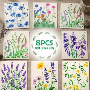 May include: A set of eight square Swedish dishcloths featuring various botanical illustrations of blue cornflowers, pink and orange wildflowers, purple bellflowers, lavender, and yellow blossoms, with the text 8PCS Soft (when wet) in the center.