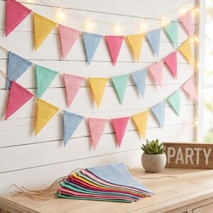 May include: A bunting banner featuring triangular flags in pastel shades of pink, yellow, blue, and green, made of a textured fabric. The banner is displayed in three horizontal rows with string lights, and a stack of matching flags sits below.