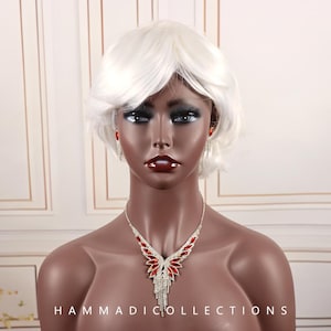 May include: A silver necklace and earring set with red and clear crystals. The necklace features a wing-like design with red crystals and dangling clear crystals. The earrings are dangling with red crystals. The mannequin has a white wig.