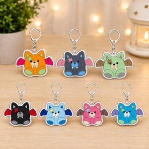 May include: A collection of colorful bat-shaped keychains. Each keychain features a cartoon bat design with a star accent and a silver keyring. The keychains are in various colors, including orange, black, blue, pink, and green.