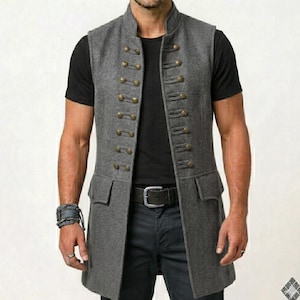 May include: A long, grey vest with a high collar and a double-breasted design. It has numerous gold-coloured buttons and two front pockets. The vest is worn over a black t-shirt and dark trousers. A black belt with a silver buckle is visible.