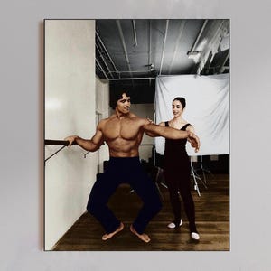 May include: A framed photograph showing a man and a woman in a dance studio. The man, shirtless, is wearing dark blue trousers and holding a ballet barre. The woman is wearing a dark dress. The background includes a white backdrop and studio equipment.