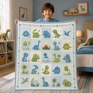 Op de afbeelding: Een rechthoekige babydeken met een raster van vijfentwintig vierkanten, elk met een kleurrijke cartoon-dinosaurus, een vulkaan of een palmboom. De lichtblauwe rand is versierd met een delicaat rankpatroon en kleine blauwe bloemetjes.