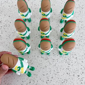 May include: A collection of ten small Subway-themed figurines, each featuring a tan bread-shaped head with a red stripe, a white shirt with the green and yellow Subway logo, and green arms and legs. The figures are arranged in a grid pattern.